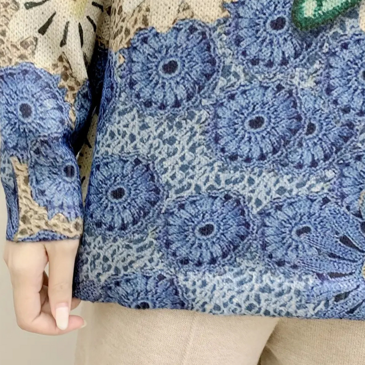 Blauwe gebreide trui met bloemmotief, close-up van mouw en hand. Modieuze dameskleding, herfst-winter collectie, comfortabele en stijlvolle outfit.