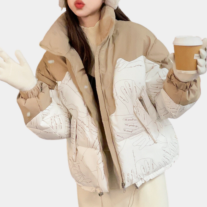 Vrouw in modieuze beige en witte gewatteerde jas met abstracte print, draagt een mok koffie en witte handschoenen. Winterkleding, trendy jas.