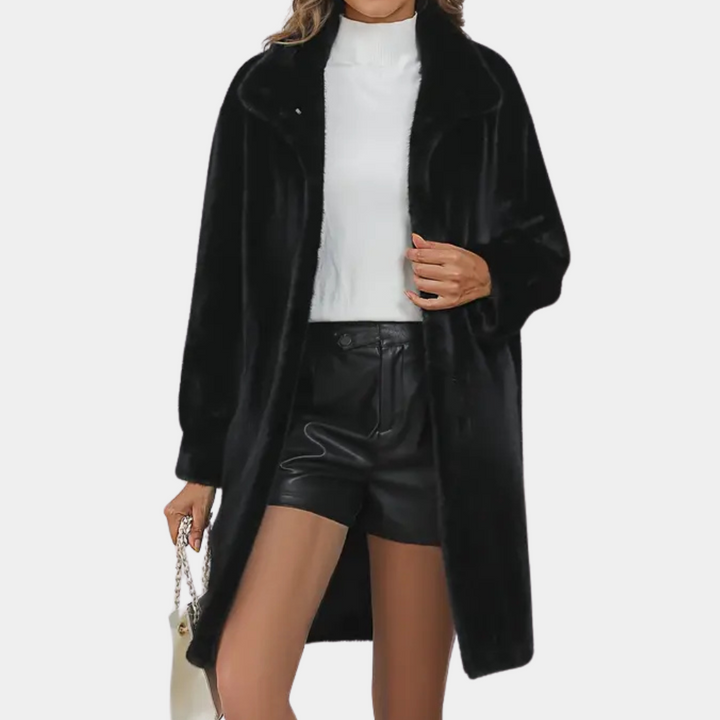 Vrouw in zwarte faux fur jas, witte trui en zwarte leren shorts, met witte handtas. Modieuze winteroutfit, trendy dameskleding.
