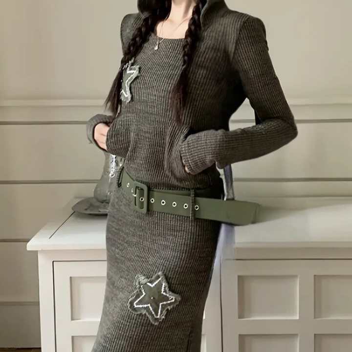 Vrouw in gebreide jurk met sterapplicaties, groene riem, lange mouwen en vlechten. Modieuze winterkleding, trendy damesmode, stijlvolle outfit.