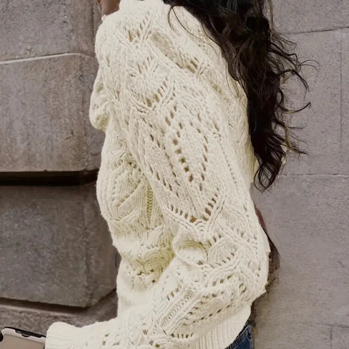 Vrouw in gebreide crèmekleurige trui met kabelpatroon, buiten bij stenen muur. Modieuze herfstkleding, warme damestrui, casual stijl.