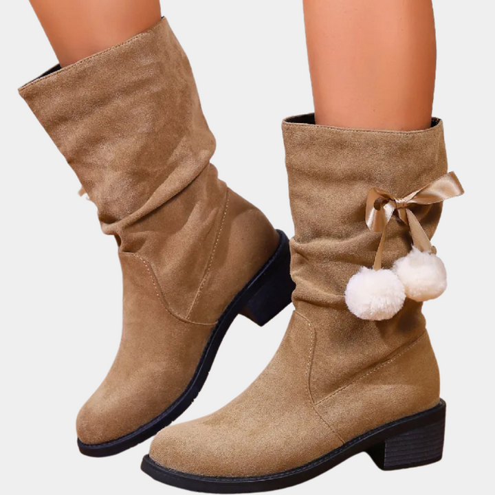 Beige suède laarzen met lage hak, pompons en strikdetail. Trendy damesmode, comfortabele winterlaarzen, stijlvol en veelzijdig.