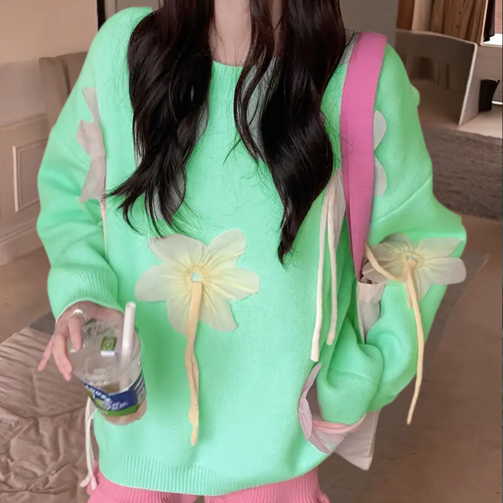 Vrouw in mintgroene trui met bloemenprint, draagt roze tas en houdt een drankje vast. Trendy damesmode, casual outfit, kleurrijke kledingstijl.