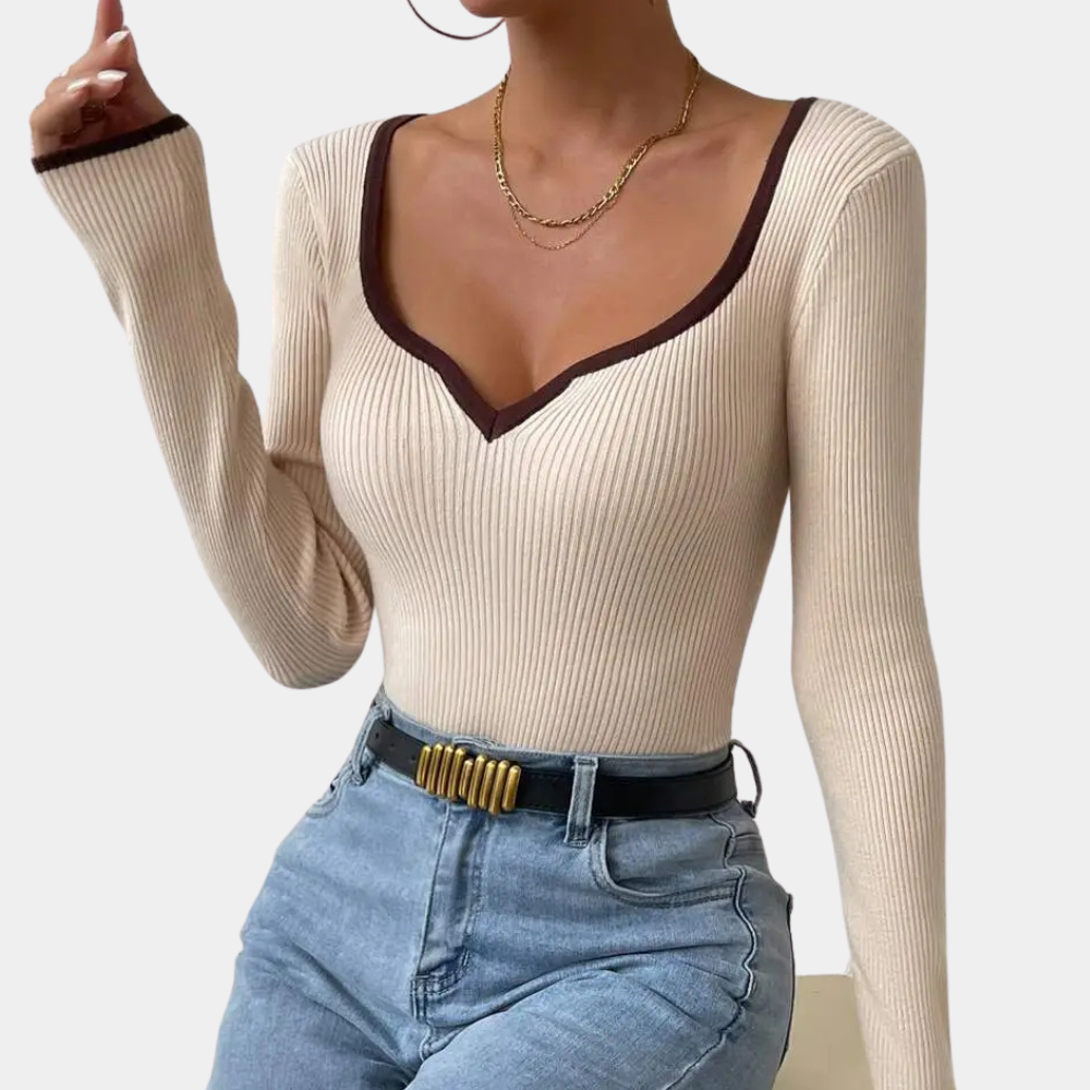 Vrouw in beige geribbelde trui met V-hals en bruine rand, gouden ketting, blauwe jeans en zwarte riem. Modieuze dameskleding, herfststijl.