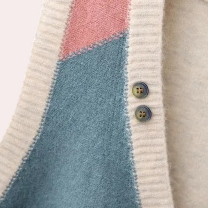 Close-up van een kleurrijke gebreide trui met geometrisch patroon in roze, blauw en wit, en twee knopen. Perfect voor herfstmode en winterstijl.