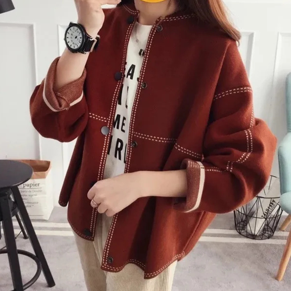 Vrouw draagt een stijlvolle bruine oversized jas met witte stiksels, gecombineerd met een casual T-shirt en horloge. Trendy herfstmode.