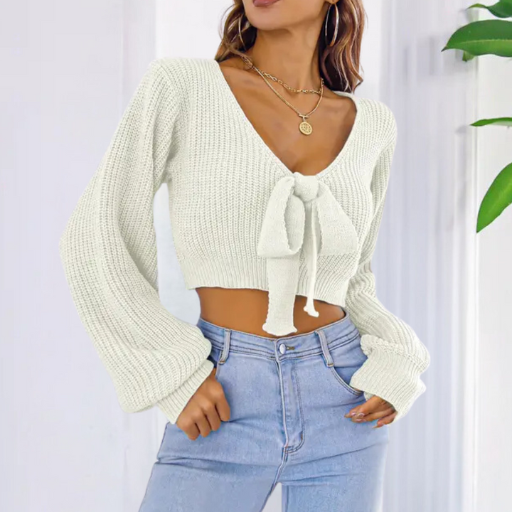 Vrouw draagt gebreide witte trui met strik en V-hals, gecombineerd met lichtblauwe jeans. Modieuze dameskleding, casual stijl.