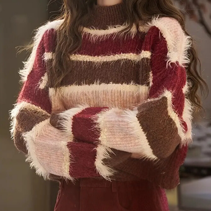 Vrouw in warme, gebreide trui met rood, roze en bruine strepen, perfect voor herfstmode. Stijlvolle dameskleding, comfortabele wintertrui.