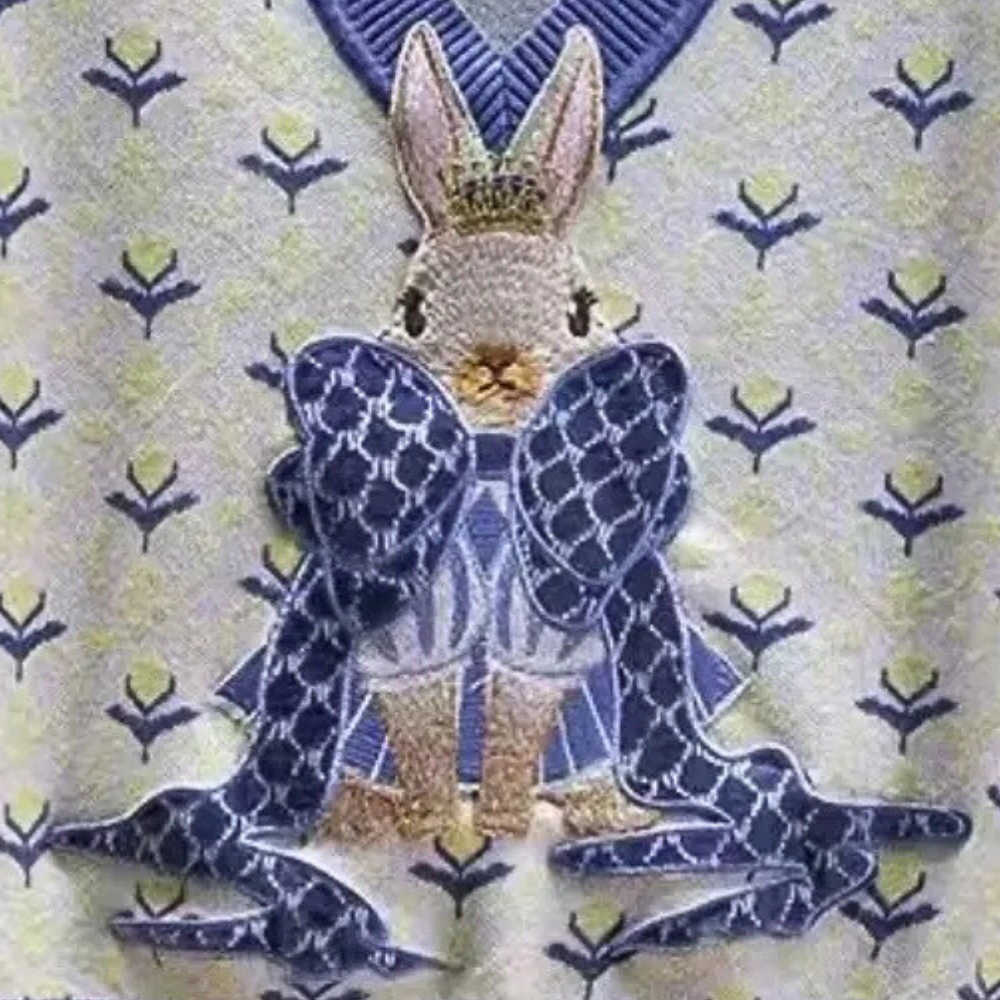 Konijn met kroon en blauwe strik op geborduurde stof met bloemenpatroon, luxe design, decoratieve textielkunst, koninklijk thema.