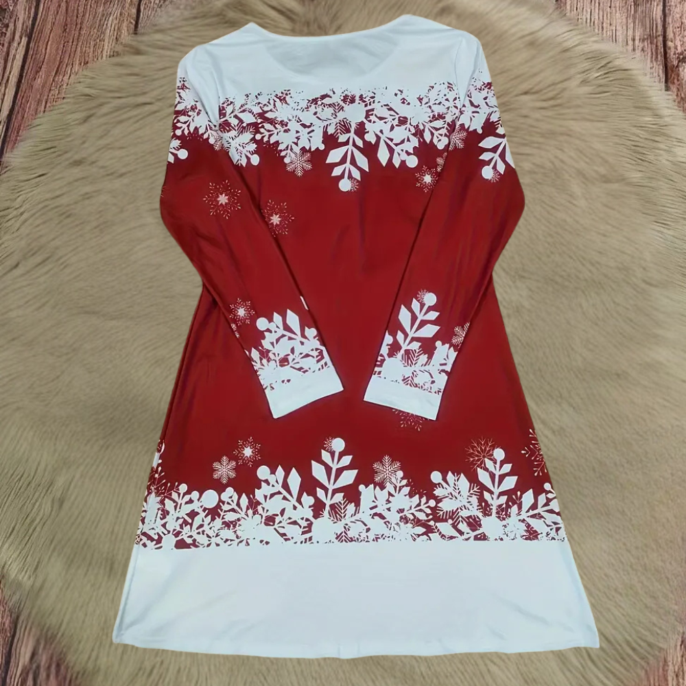 Rode kerstjurk met lange mouwen, versierd met witte sneeuwvlokken en bladeren, liggend op een beige vloerkleed. Perfect voor feestelijke gelegenheden.