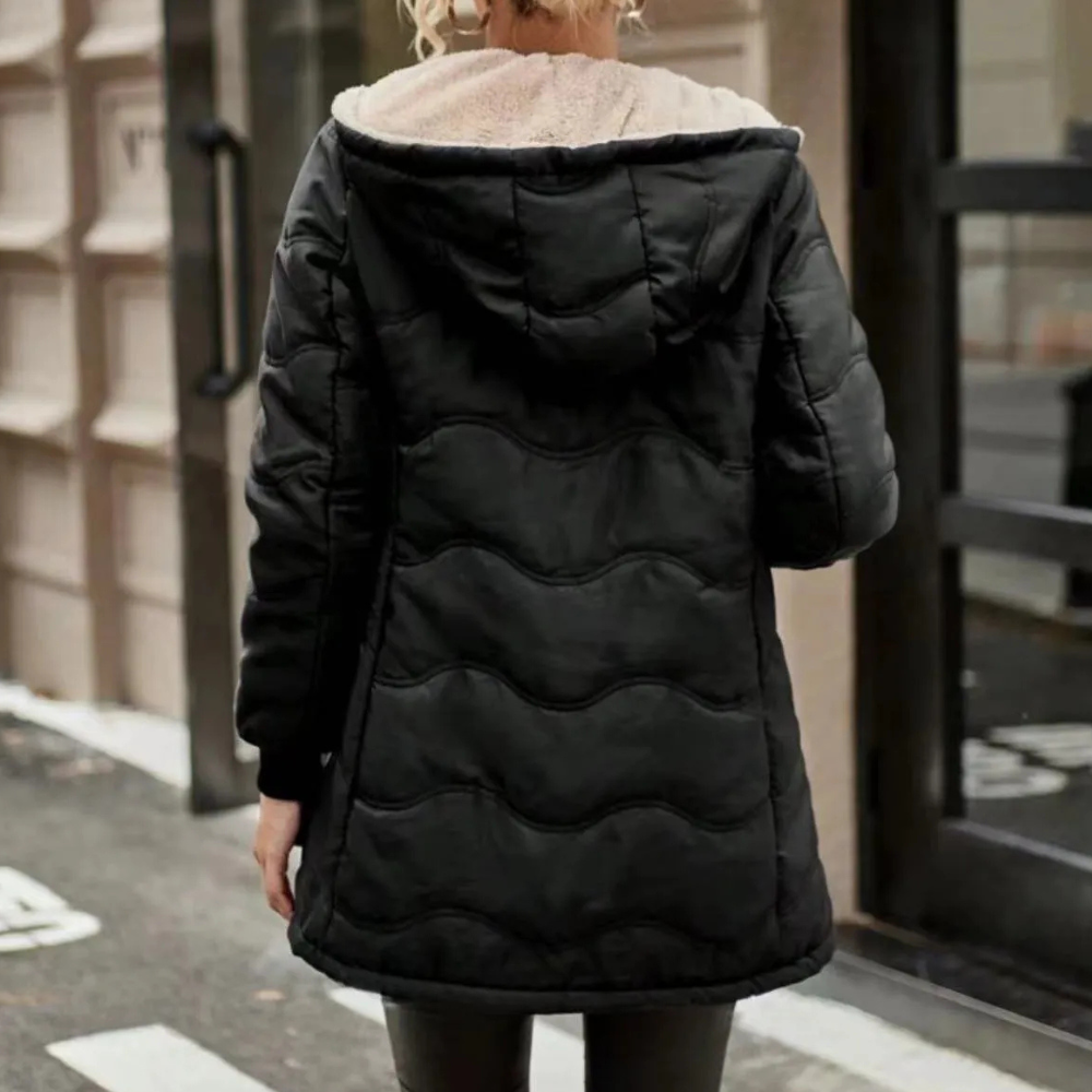 Zwarte gewatteerde winterjas met capuchon, gedragen door een persoon op straat. Stijlvolle en warme damesjas voor koude seizoenen.