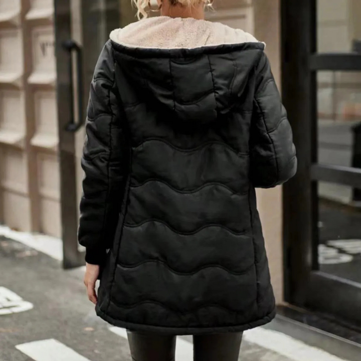 Zwarte gewatteerde winterjas met capuchon, gedragen door een persoon op straat. Stijlvolle en warme damesjas voor koude seizoenen.