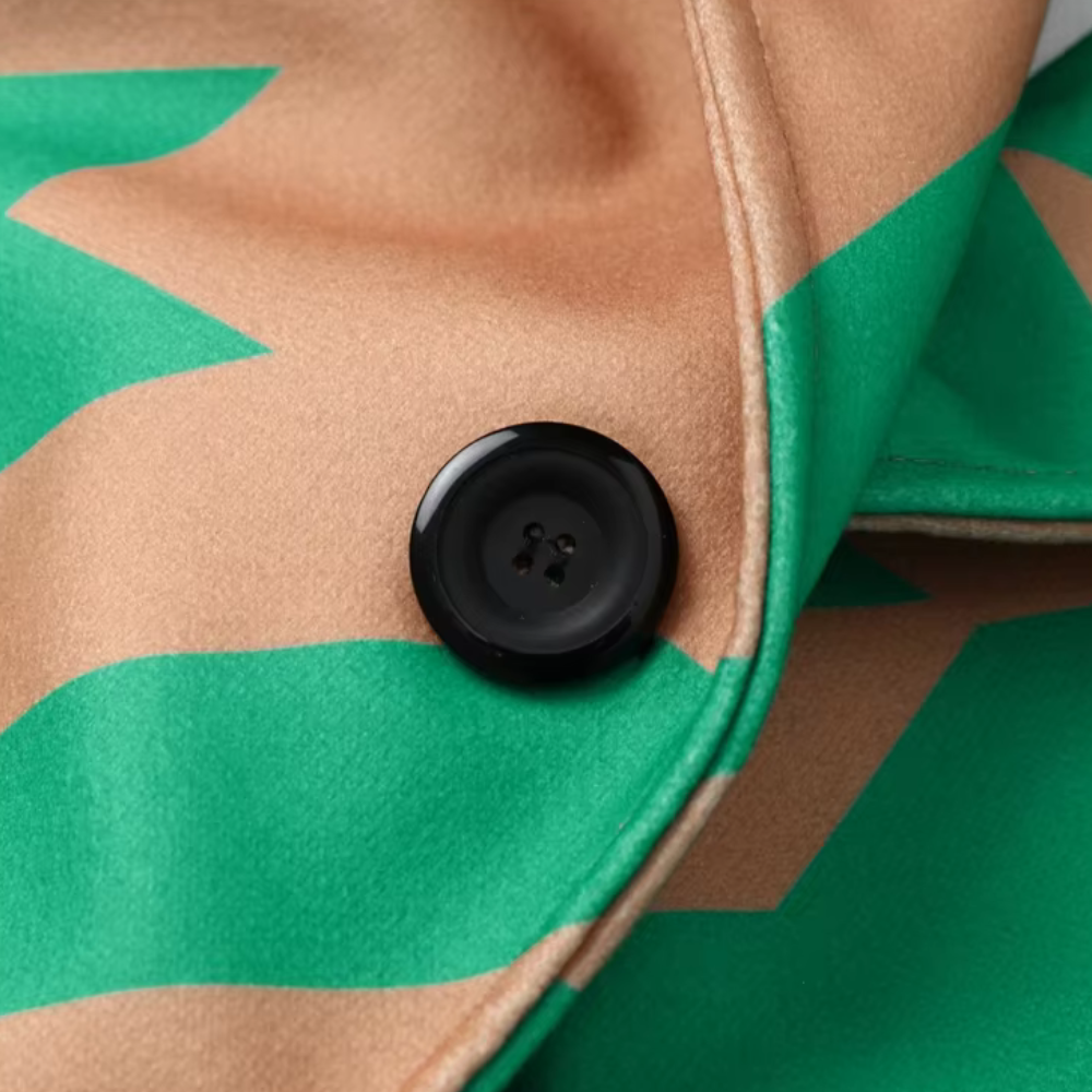Beige en groene jas met zigzagpatroon en zwarte knoop, close-up. Modieuze dameskleding, trendy herfstjas, stijlvolle knoopdetails.