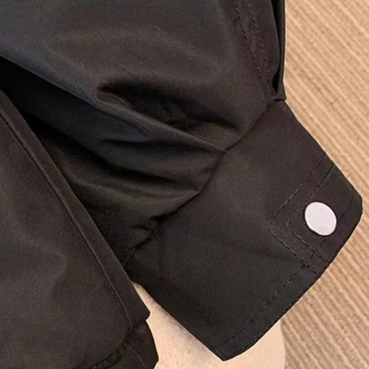 Zwarte gewatteerde jas met knoopsluiting op mouw, close-up. Modieuze winterkleding, warme jas, duurzame stof, stijlvolle afwerking.