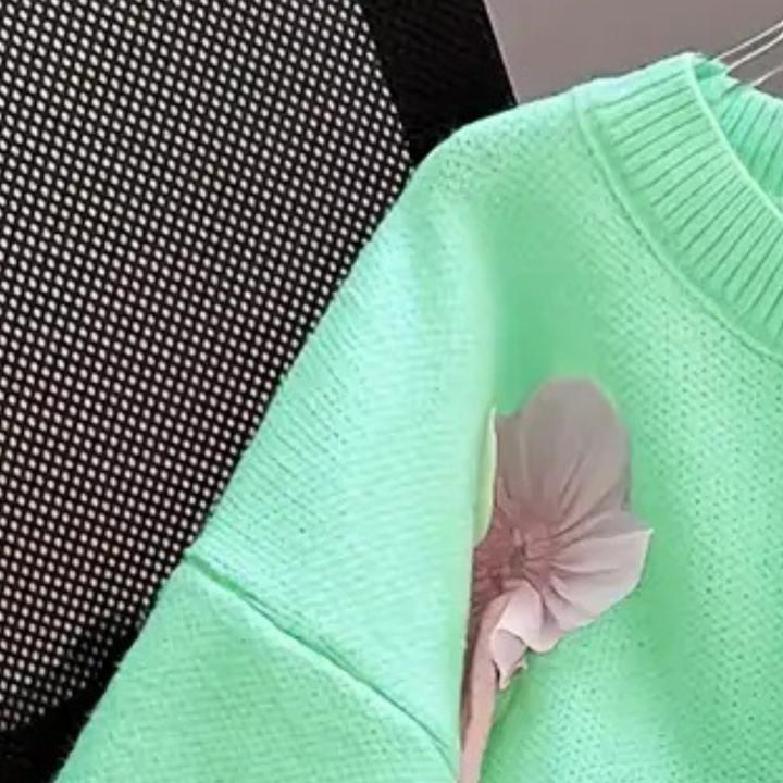 Mintgroene trui met bloemdetail op rugleuning van zwarte stoel, gebreide textuur, trendy damesmode, stijlvolle kledingaccessoire.
