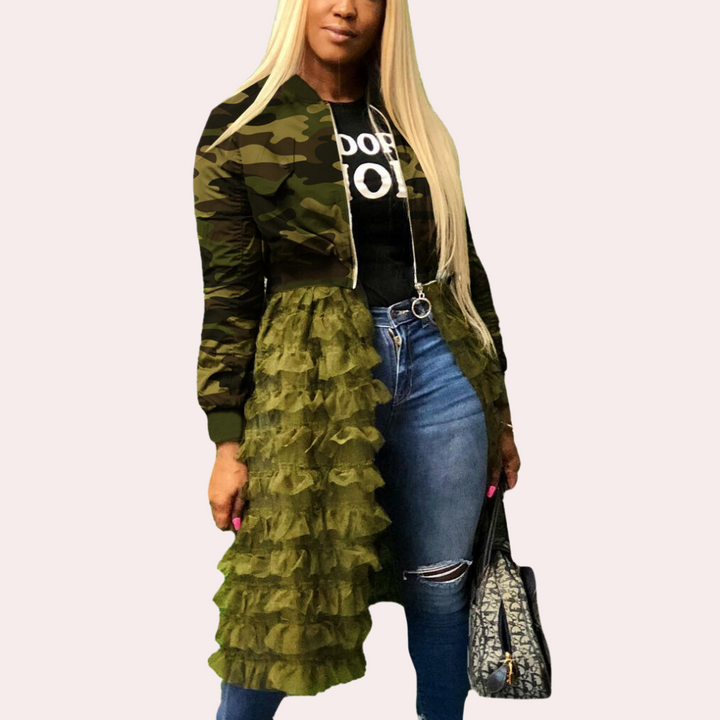 Vrouw in camouflagejack met groene ruches, blauwe jeans en zwarte top, draagt designer handtas. Modieuze streetwear outfit.