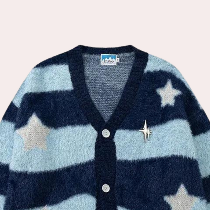 Blauwe en witte gestreepte cardigan met sterrenpatroon, gemaakt van pluizige stof. Voorzien van knopen en een decoratieve sterspeld.