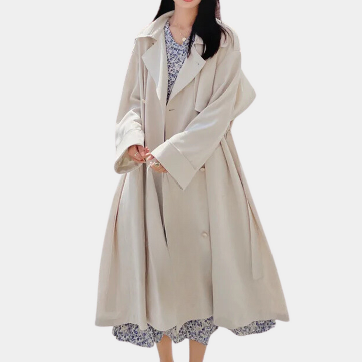 Vrouw in oversized beige trenchcoat over bloemenjurk, modetrend herfst 2023, stijlvolle dameskleding, casual chique outfit, witte achtergrond.