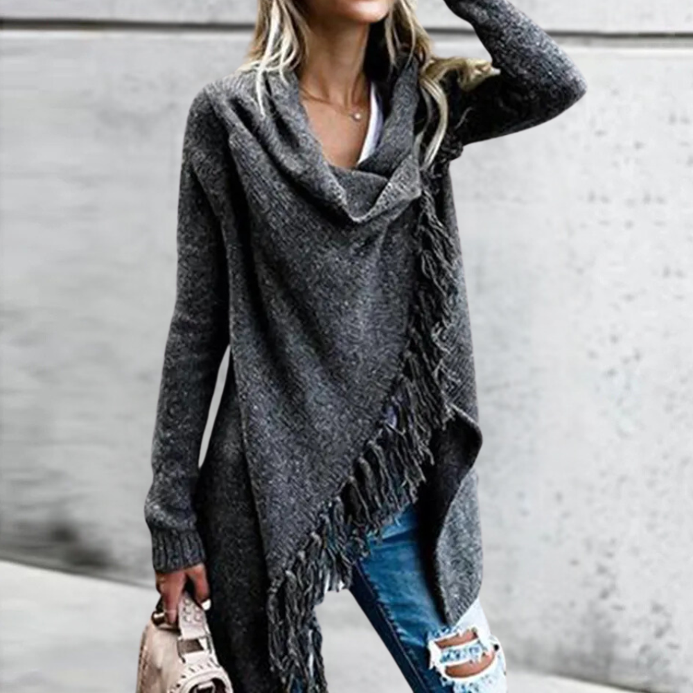 Vrouw in grijze asymmetrische trui met franjes, draagt gescheurde jeans en beige tas. Modieuze herfstkleding, casual damesoutfit.