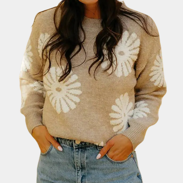 Vrouw in beige trui met witte bloemenprint, casual stijl, handen in zakken van blauwe jeans. Perfect voor herfstmode en trendy dameskleding.