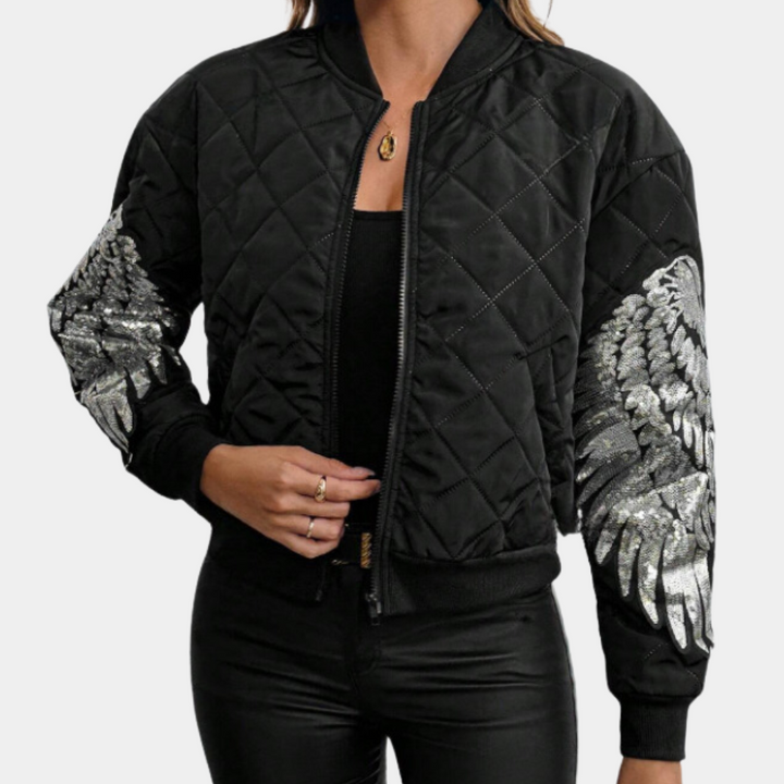 Zwarte gewatteerde bomberjack met zilveren vleugelmotief op mouwen, gedragen door vrouw. Modieuze damesjas, trendy streetwear.