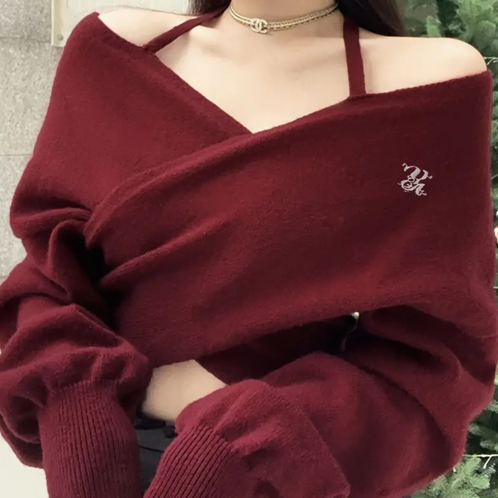 Vrouw in bordeauxrode off-shoulder trui met lange mouwen en choker, voor kerstboom. Modieuze winterkleding, trendy damesmode.