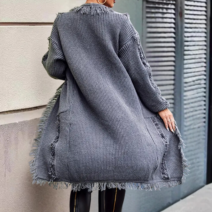 Grijze oversized gebreide trui met franjes, gedragen door een model. Perfect voor herfstmode, casual en stijlvol. Comfortabele dameskleding.