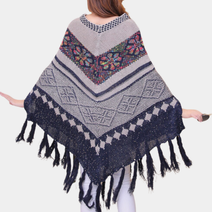 Vrouw draagt kleurrijke gebreide poncho met bloemenpatroon en franjes, bohemian stijl, wintermode, warme dameskleding, trendy accessoire.