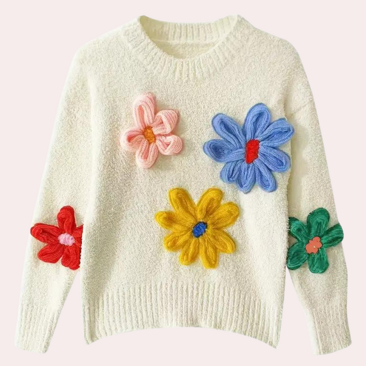 Witte trui met kleurrijke gebreide bloemenapplicaties, waaronder roze, blauwe, gele en groene bloemen. Trendy damesmode, herfstkleding.