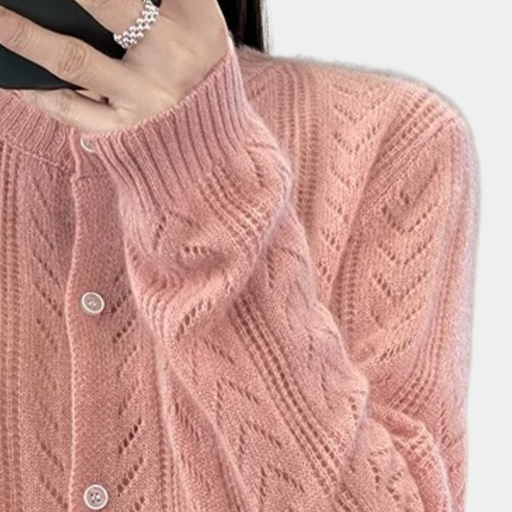 Roze gebreid vest met knoopsluiting, gedragen door persoon met zilveren ring. Modieuze dameskleding, herfstmode, zachte textuur.