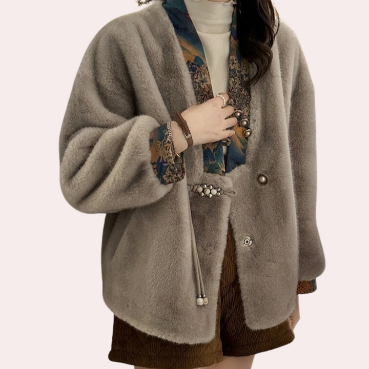 Grijze faux fur jas met kleurrijke sjaalkraag, gedragen door een vrouw. Modieuze winterjas, elegant design, warme dameskleding.