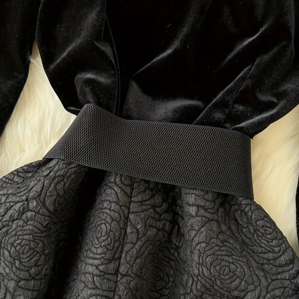 Zwarte fluwelen jurk met brede tailleband en gebloemd patroon op de rok, elegant avondkledingontwerp, perfect voor formele gelegenheden.