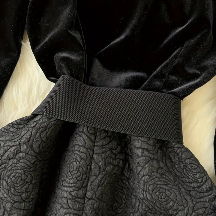 Zwarte fluwelen jurk met brede tailleband en gebloemd patroon op de rok, elegant avondkledingontwerp, perfect voor formele gelegenheden.