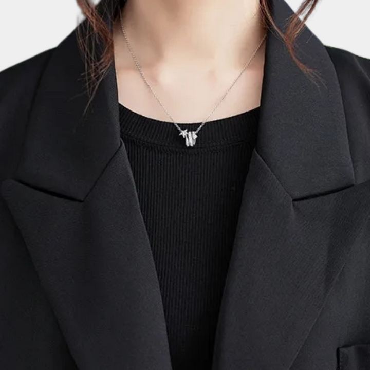 Zilveren vlinderhanger ketting op zwarte trui en blazer. Elegante damesmode, minimalistisch design, stijlvolle sieradenaccessoire.
