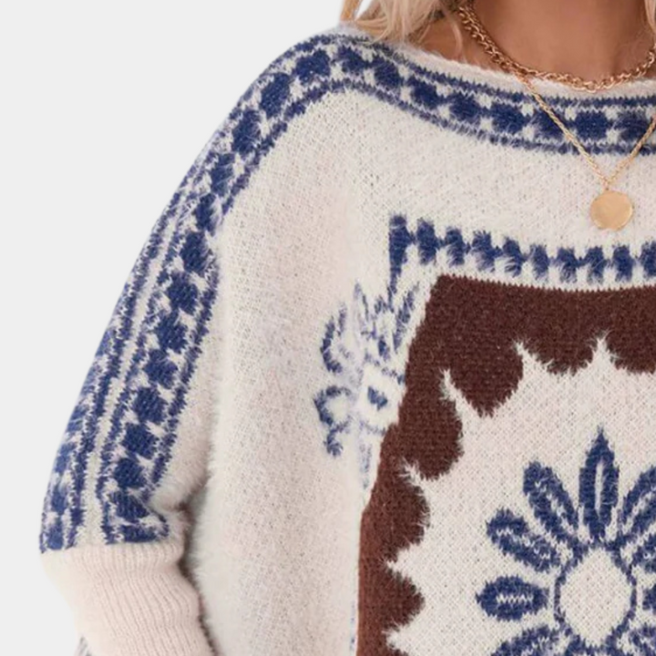 Witte trui met blauwe en bruine Noorse print, ronde hals en gouden ketting. Perfect voor wintermode en Scandinavische stijl.