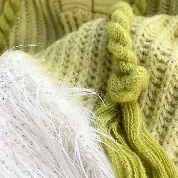 Groene gebreide trui met kabelpatroon en witte pluizige details, close-up. Perfect voor wintermode en warme kleding.