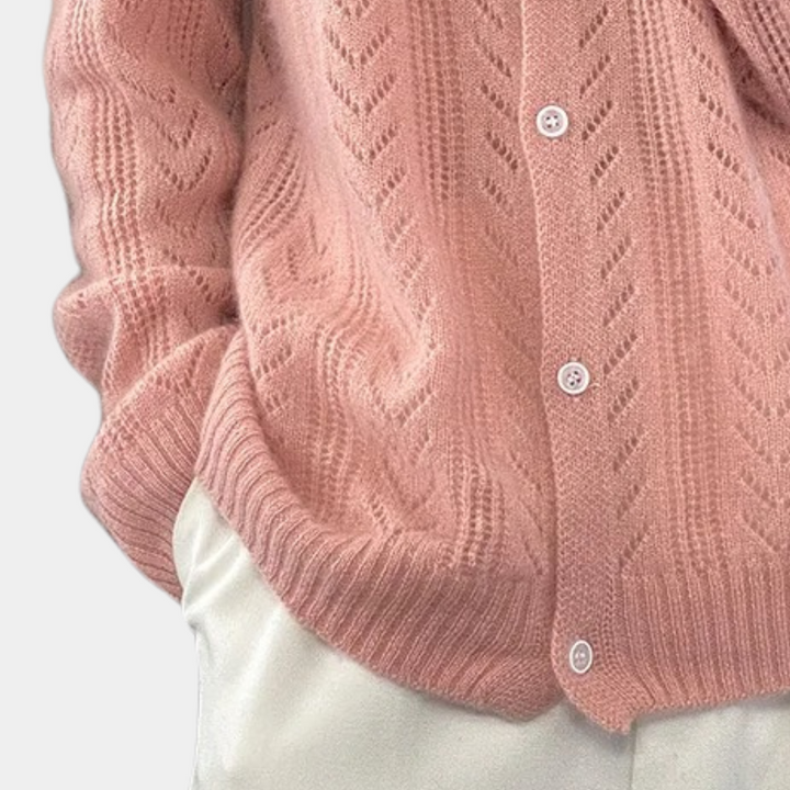 Roze gebreid vest met kabelpatroon en witte knopen, gedragen over een witte broek. Stijlvolle damesmode, herfstkleding, comfortabele outfit.