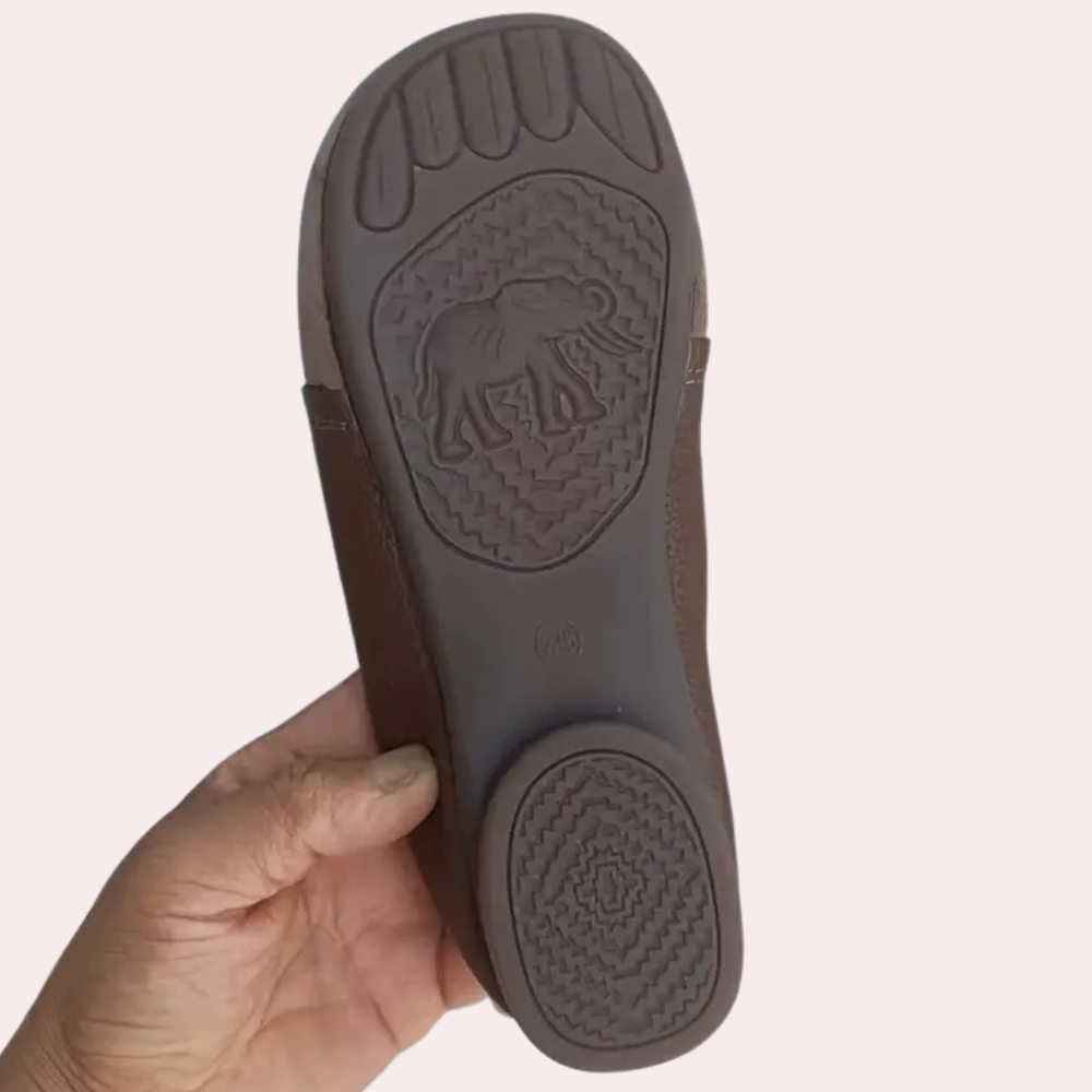 Bruine leren sandaal met olifantengrip op de zool, vastgehouden door een hand. Comfortabele, duurzame sandalen voor dagelijks gebruik.
