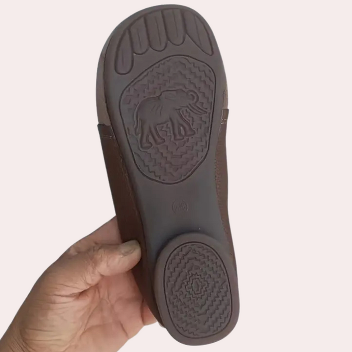Bruine leren sandaal met olifantengrip op de zool, vastgehouden door een hand. Comfortabele, duurzame sandalen voor dagelijks gebruik.