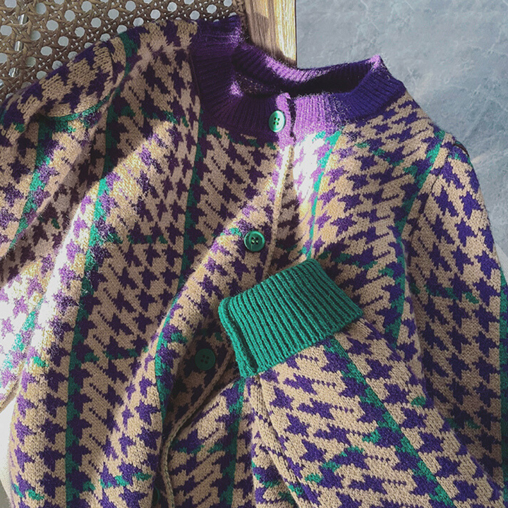 Vintage gebreid vest met paarse en groene ruitpatronen, houten knopen en geribbelde boorden, liggend op een rieten stoel. Retro mode, herfstkleding.