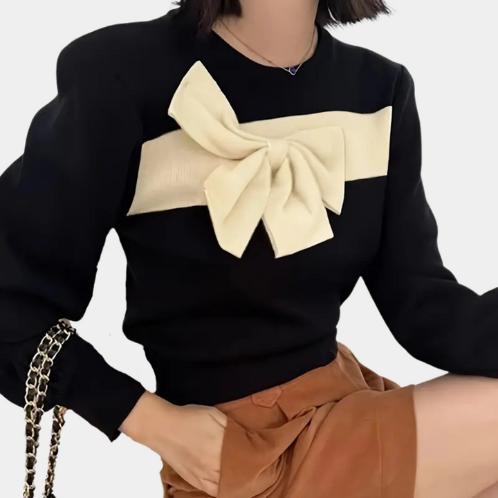 Vrouw draagt zwarte trui met grote crèmekleurige strik, gecombineerd met bruine rok. Modieuze dameskleding, herfstoutfit, stijlvolle trui.