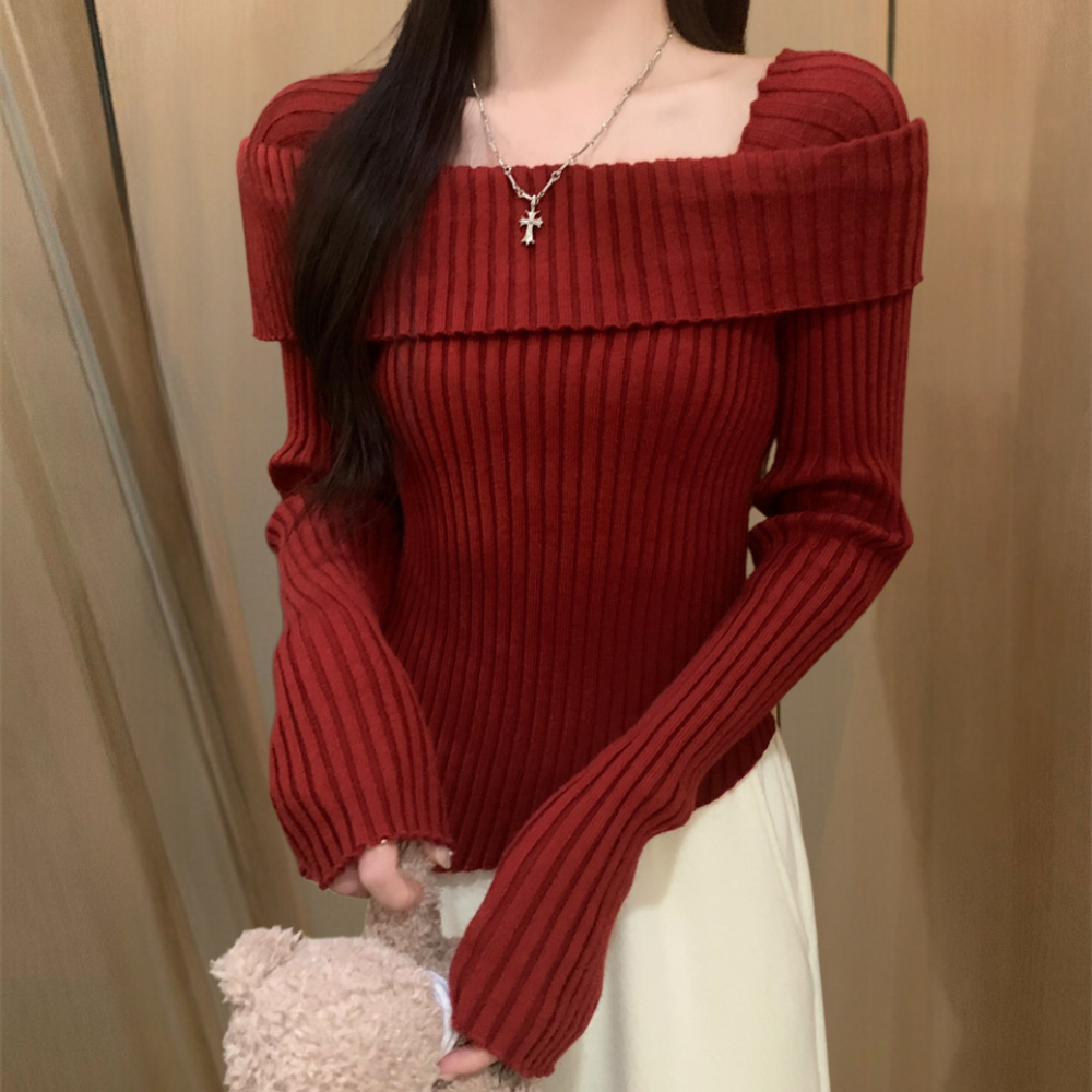 Vrouw in rode, geribbelde off-shoulder trui met kruis ketting, houdt een teddybeer vast. Modieuze dameskleding, herfst/winter stijl.