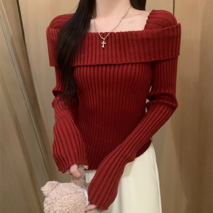 Vrouw in rode, geribbelde off-shoulder trui met kruis ketting, houdt een teddybeer vast. Modieuze dameskleding, herfst/winter stijl.