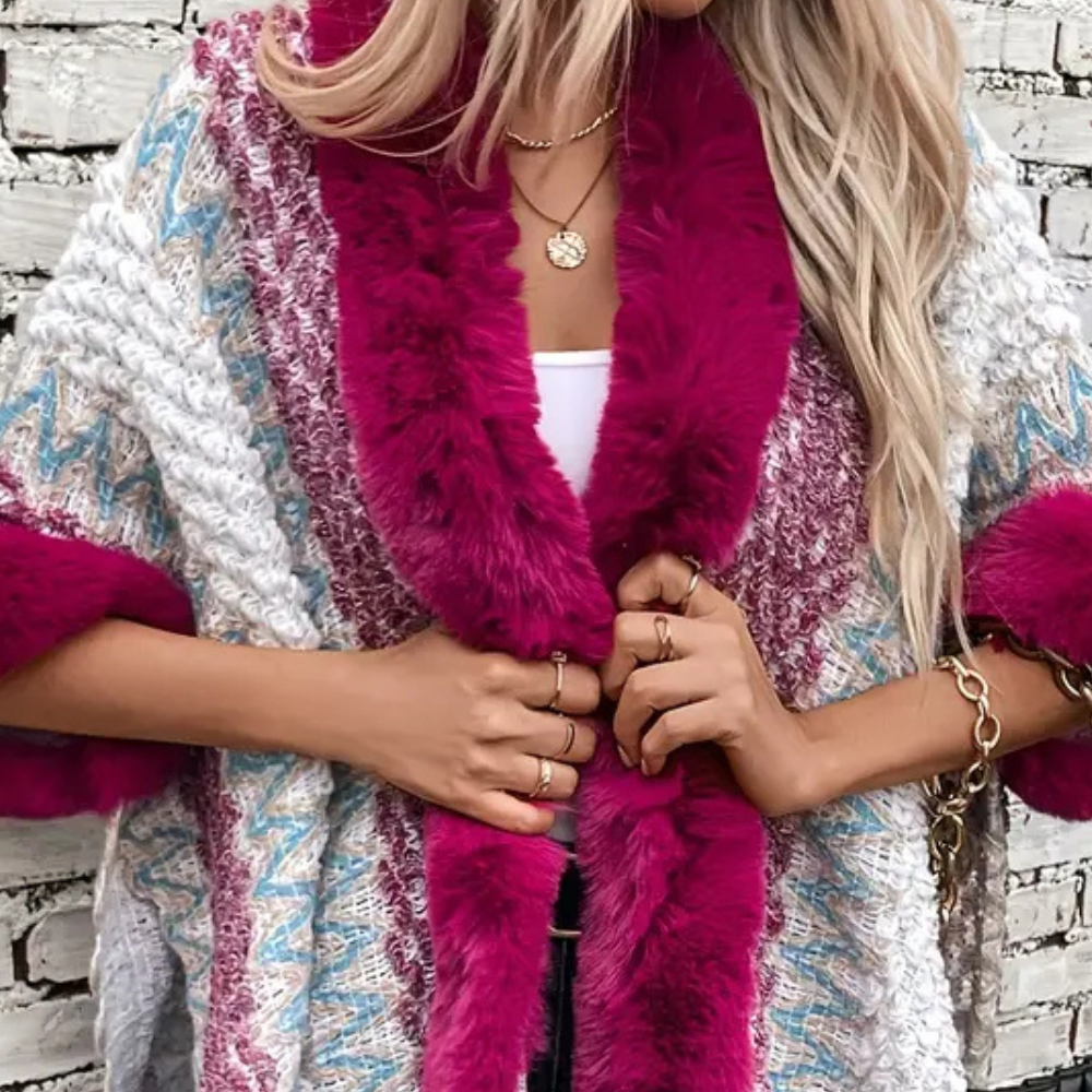 Vrouw in kleurrijke gebreide trui met roze bontkraag, witte top, gouden sieraden, tegen bakstenen muur. Modieuze herfstkleding, trendy stijl.