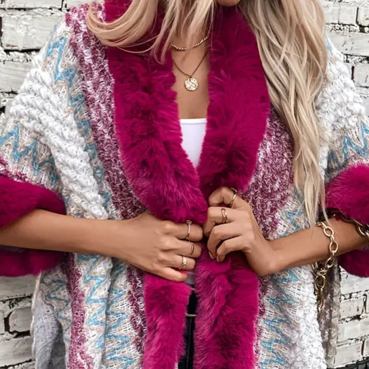 Vrouw in kleurrijke gebreide trui met roze bontkraag, witte top, gouden sieraden, tegen bakstenen muur. Modieuze herfstkleding, trendy stijl.