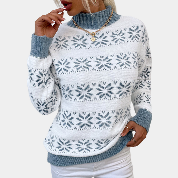 Vrouw draagt witte trui met blauw sneeuwvlokpatroon, coltrui en gouden ketting. Modieuze winterkleding, casual stijl.