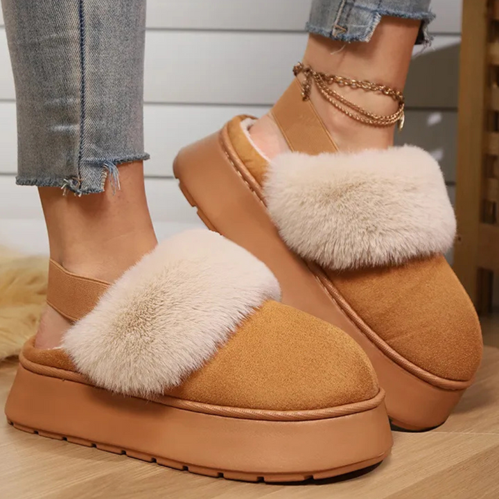 Bruine platform pantoffels met witte pluche voering, gedragen door een persoon met jeans. Trendy damesmode, comfortabele winterse schoenen.
