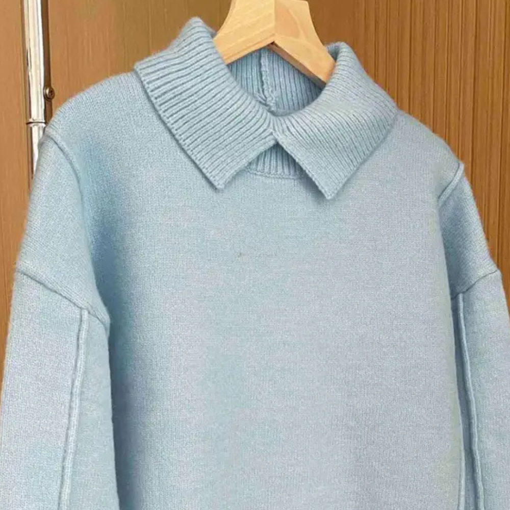 Lichtblauwe trui met brede kraag, gebreid ontwerp, hangend aan houten hanger. Perfect voor herfstmode, casual en stijlvol.