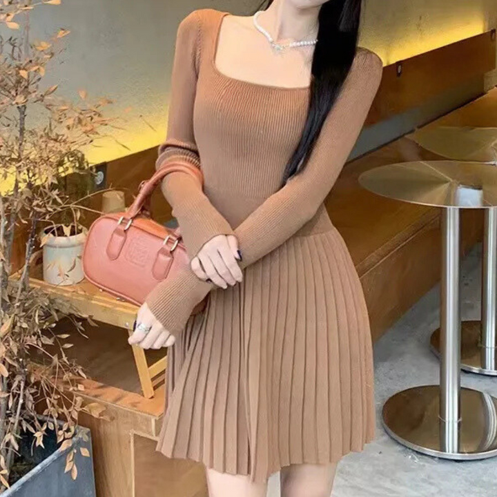 Vrouw in bruine, geribbelde jurk met lange mouwen en plissé rok, naast een roze handtas op houten bank. Stijlvolle herfstmode, elegantie.