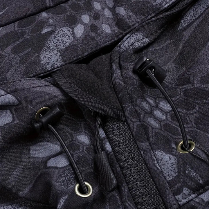 Close-up van een zwarte camouflage jas met trekkoord en ritssluiting, ideaal voor outdoor activiteiten. Waterafstotend en duurzaam materiaal.